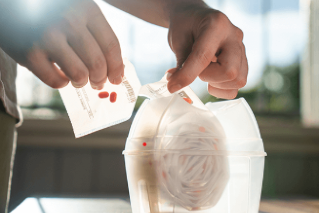 Hands tearing off a single daily dose sachet from the medication dispenser roll